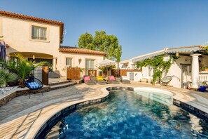 Uma piscina com espreguiçadeiras, um pergolado e um edifício com telhado em azulejos.