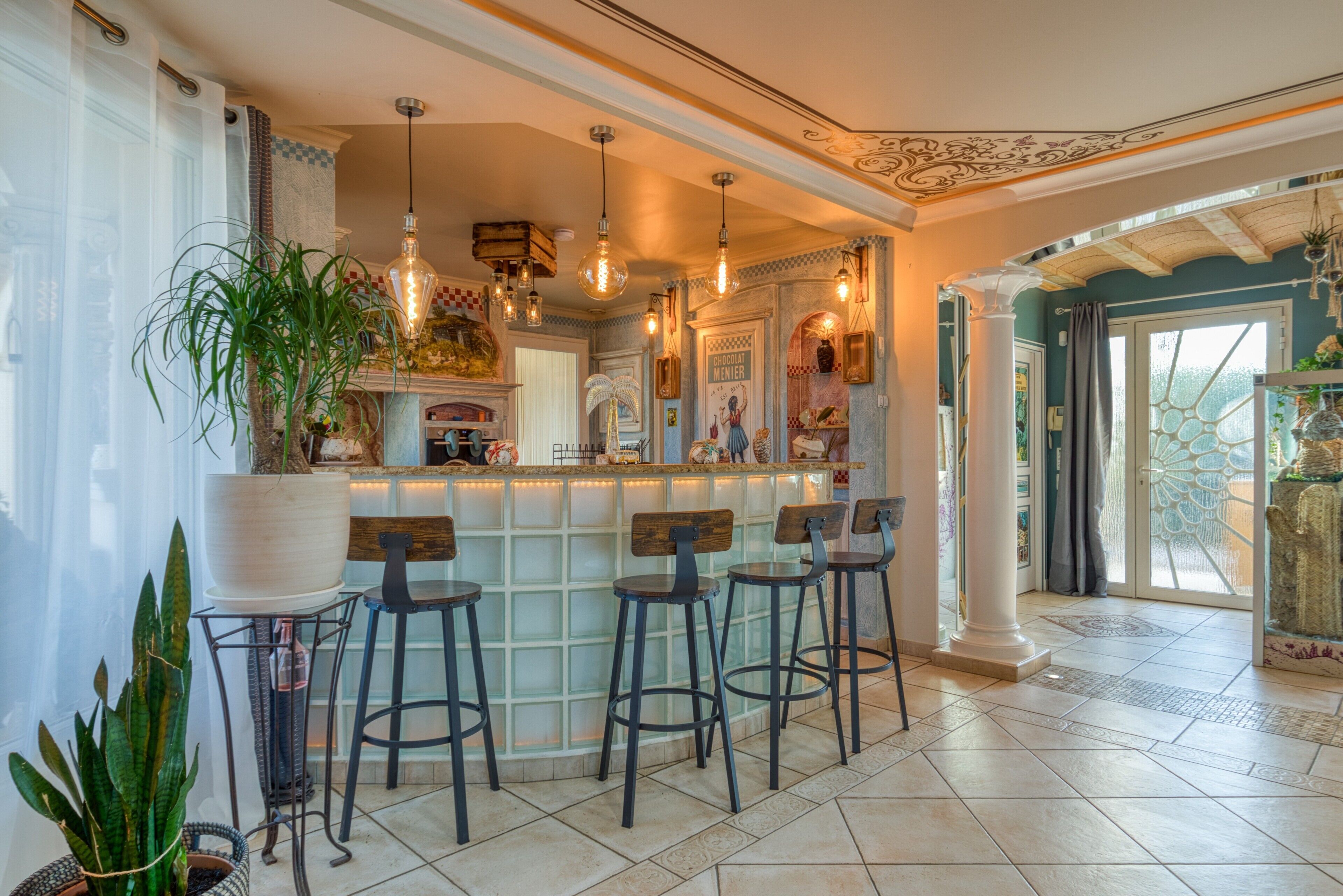 A bar area with stools and a counter, a large potted plant, and decorative lighting.