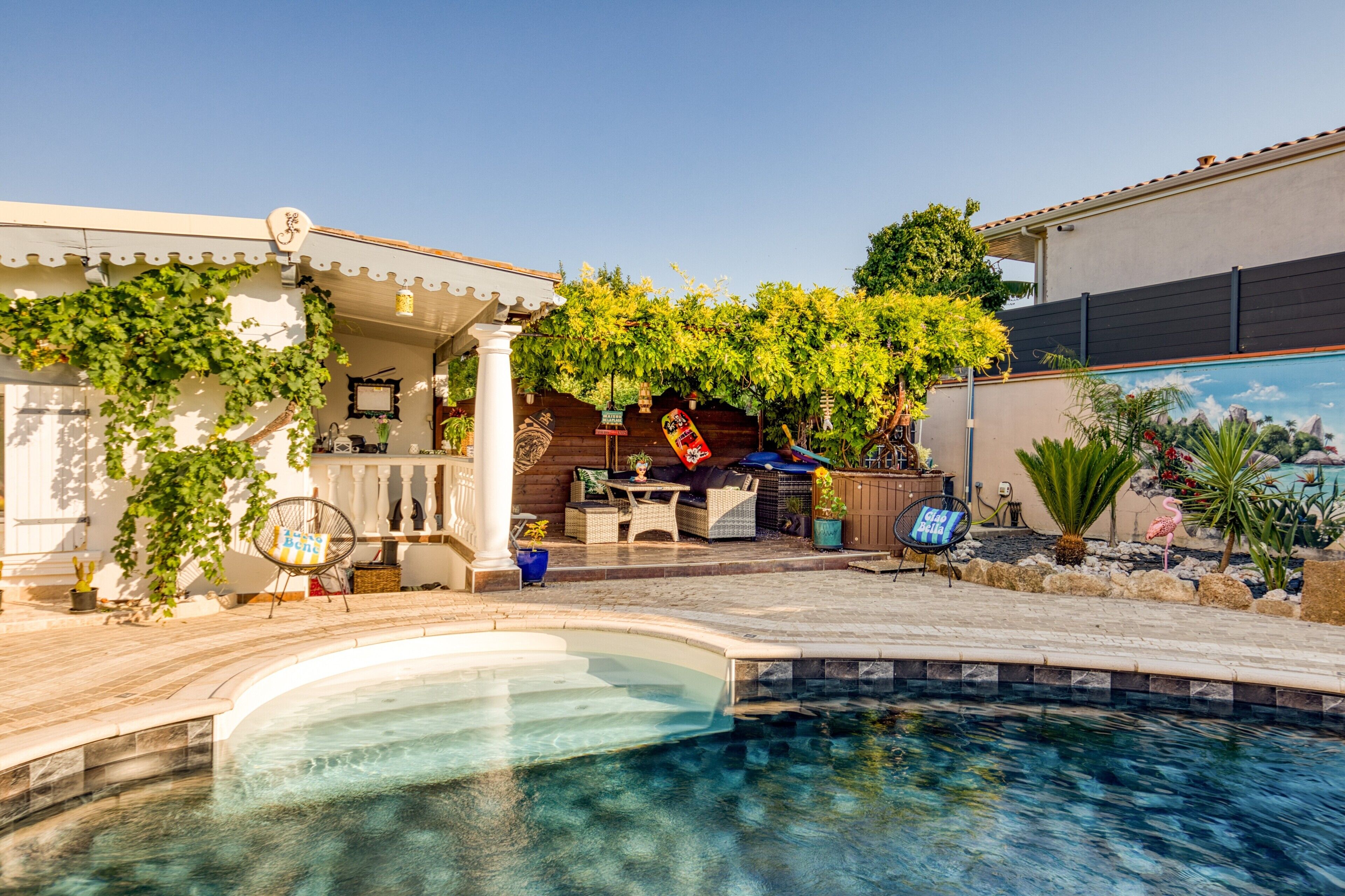 A pool area with a pergola, seating, and a mural on the adjacent wall.