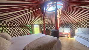 Interior de una yurta con cama, sofá y estructura de poste central.