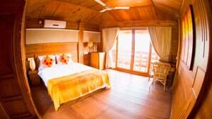 A wooden room with a bed, a ceiling fan, a window with curtains, and a wicker chair.