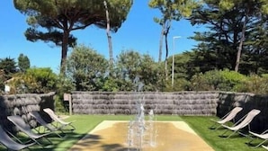 Una piscina con fuente, rodeada de sillas de descanso y un muro de piedra.