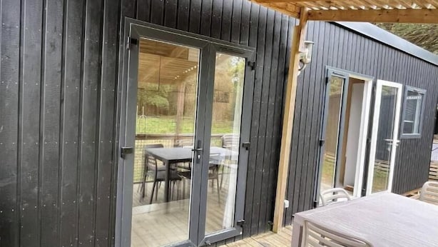 Una terraza de madera con una zona cubierta, un ventanal corredero y una mesa con sillas.