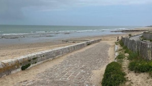 Un sendero costero que lleva a una playa, con un muro de piedra y una cerca de madera.