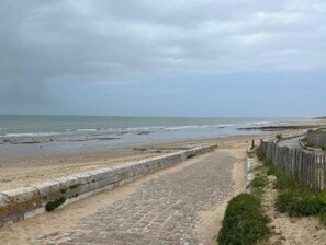 Ein Küstenpfad führt zu einem Strand mit einer Steinmauer und einem Holenzaun.