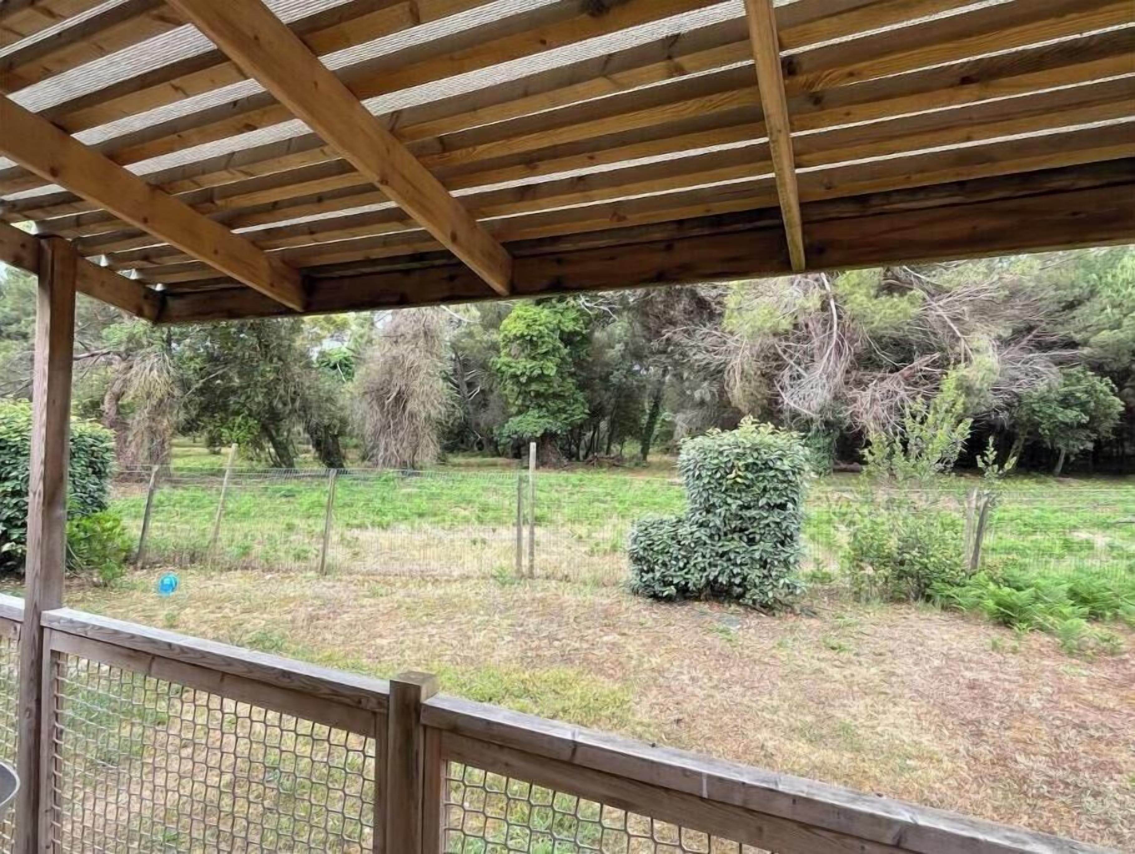 Une structure de pergola en bois offrant une vue sur un jardin clos.