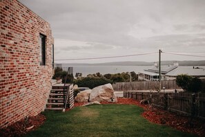A brick building with a small grassy yard, a wooden fence, and a view of the sea.
