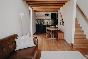 A cozy living room with a brown leather sofa, a wooden dining table, and a staircase.
