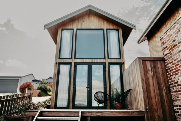 A modern two-story house with large windows, a wooden deck, and a brick wall.