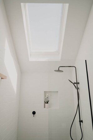A shower with a skylight, white tiled walls, and a small shelf with a plant.