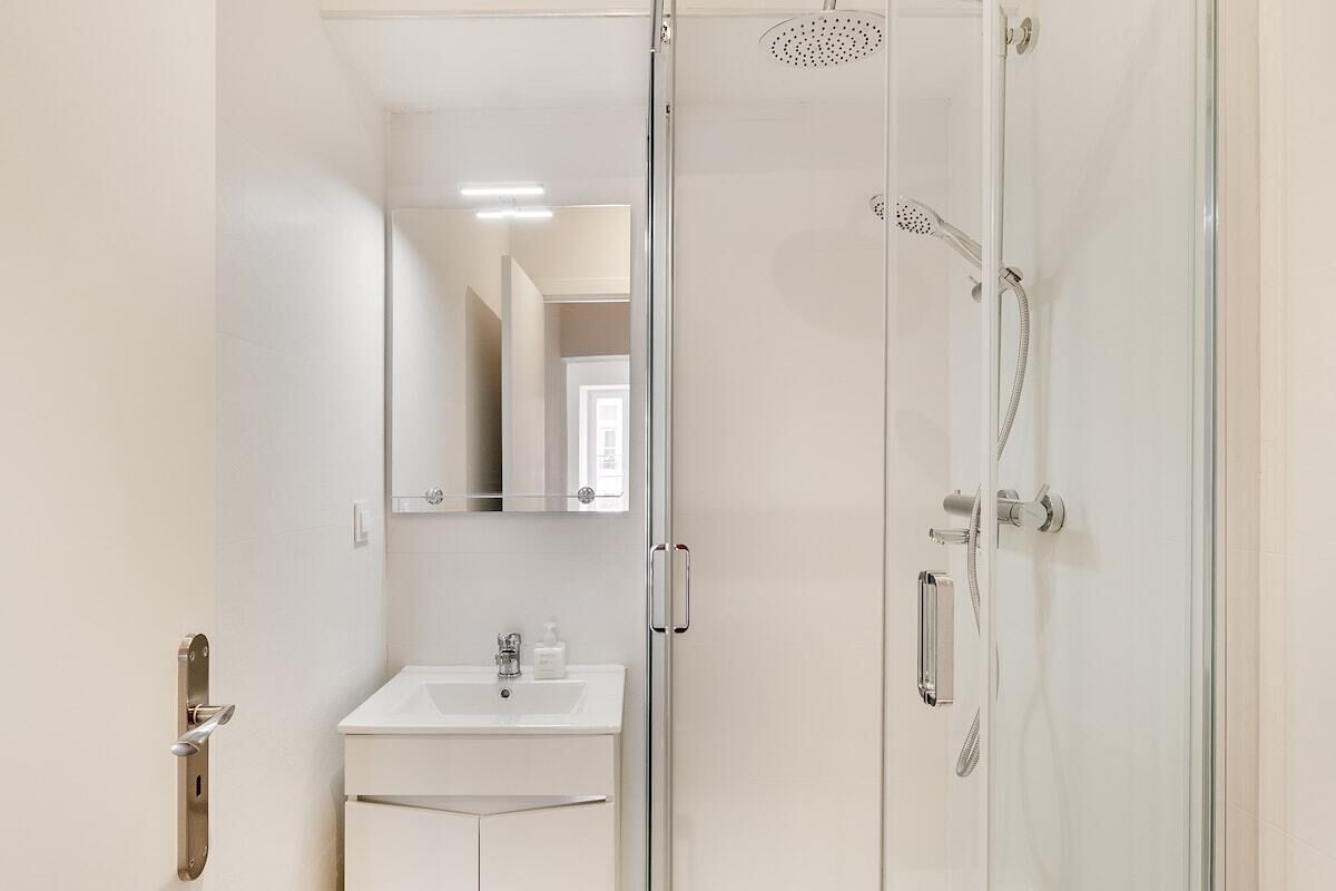 Un baño moderno con cabina de ducha de vidrio, un lavabo con espejo y una puerta con manija.