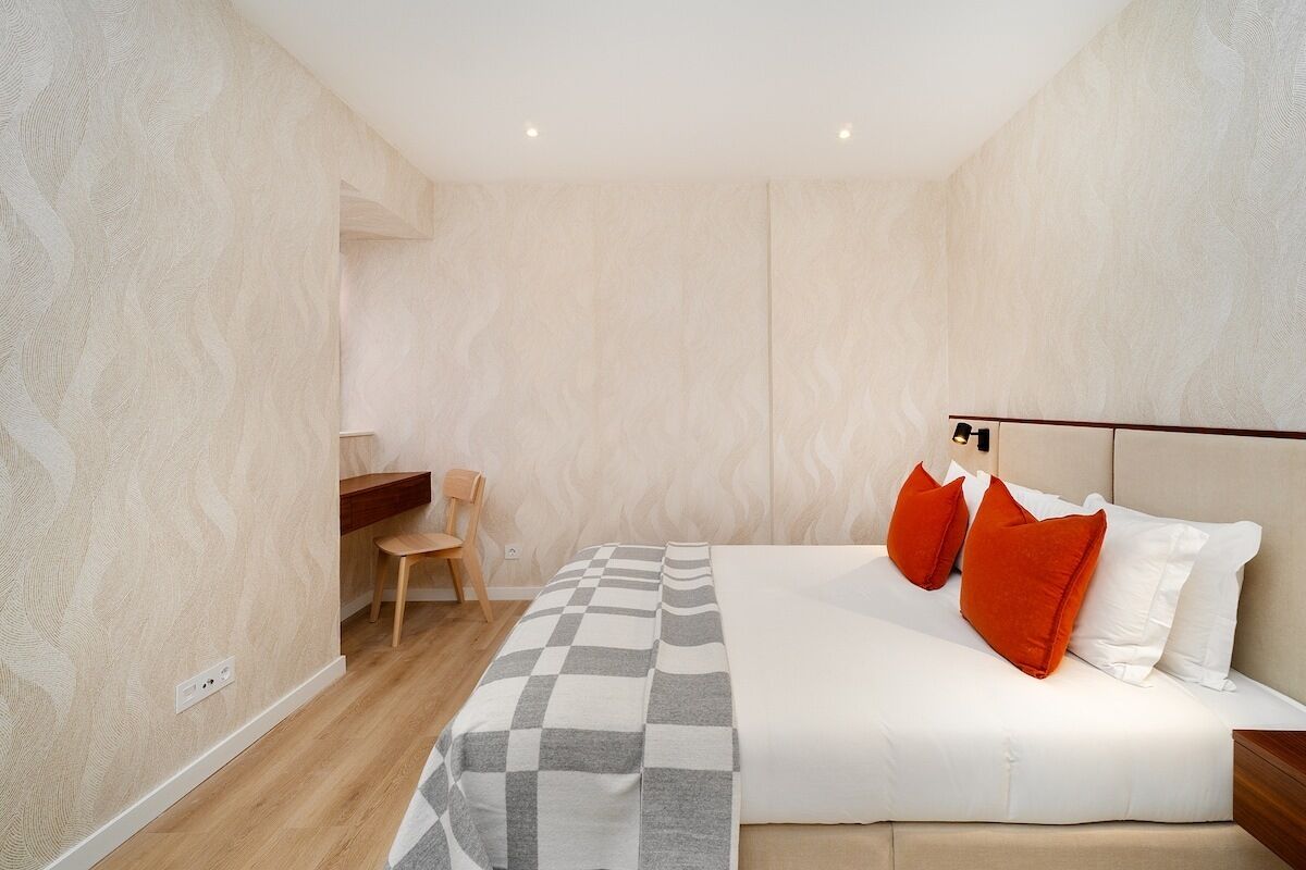 Een slaapkamer met een kamer met een geruit sprei, een houten stoel, een nachtkastje en een wandlamp.