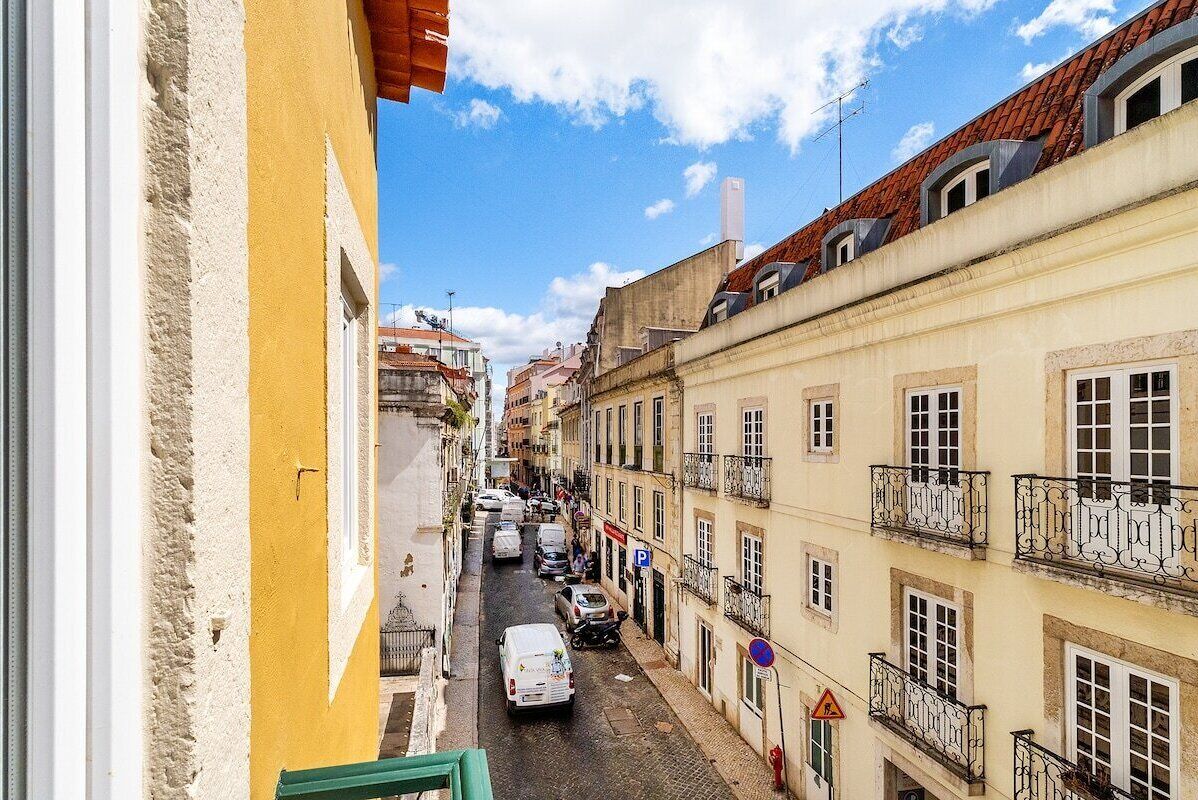 Uma rua estreita com edifícios em ambos os lados, céu claro e carros estacionados.
