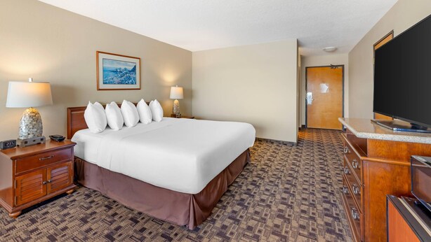 A hotel room with a large bed, two bedside lamps, a flat-screen TV, a wooden dresser, and a patterned carpet. - Newport Oceanfront Inn (Newport)