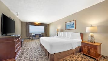 A hotel room with a large bed, a television, a desk, and a view of the ocean.