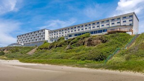 Un hotel de varios pisos con techo plano, situado en una ladera con una playa al frente.