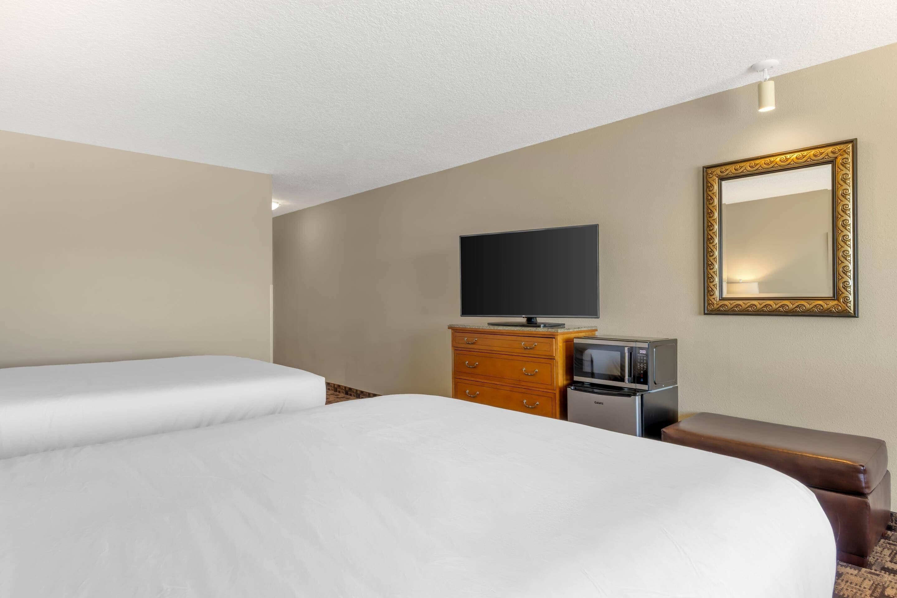 A hotel room with two beds, a television, a microwave, and a dresser.