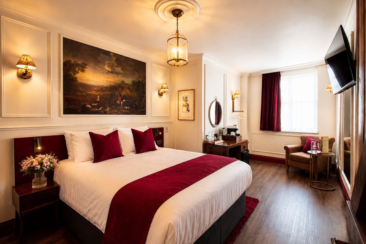 A hotel room with a large bed, a desk, a chair, a TV, and artwork on the walls.