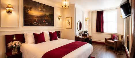 A hotel room with a large bed, a desk, a chair, a TV, and artwork on the walls.