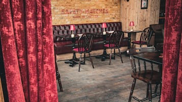 Interior acogedor de restaurante con pared de ladrillo, cortinas de terciopelo rojo, muebles de madera y un mural de una cabra.