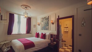 A hotel room with a bed, a nightstand, a window with curtains, a door leading to a bathroom, and a checkered floor.