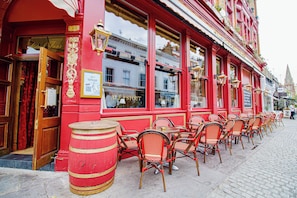 A red building with a door, windows, and outdoor seating with chairs and tables.