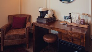 A hotel room with a wooden desk, a chair, a coffee maker, a mirror, and a small refrigerator.