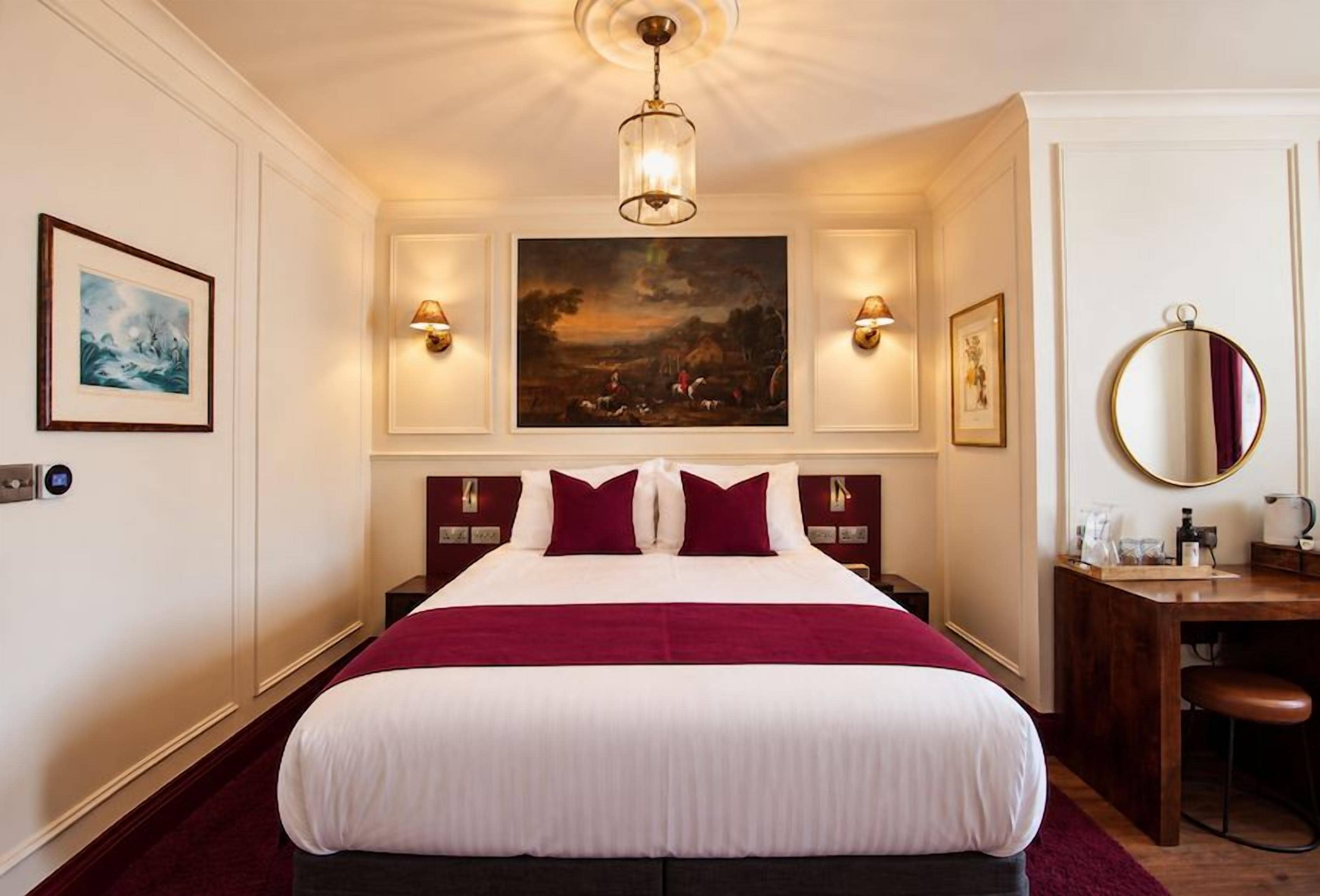 A hotel room with a large bed, two bedside tables, a desk with a chair, and a large painting above the bed.