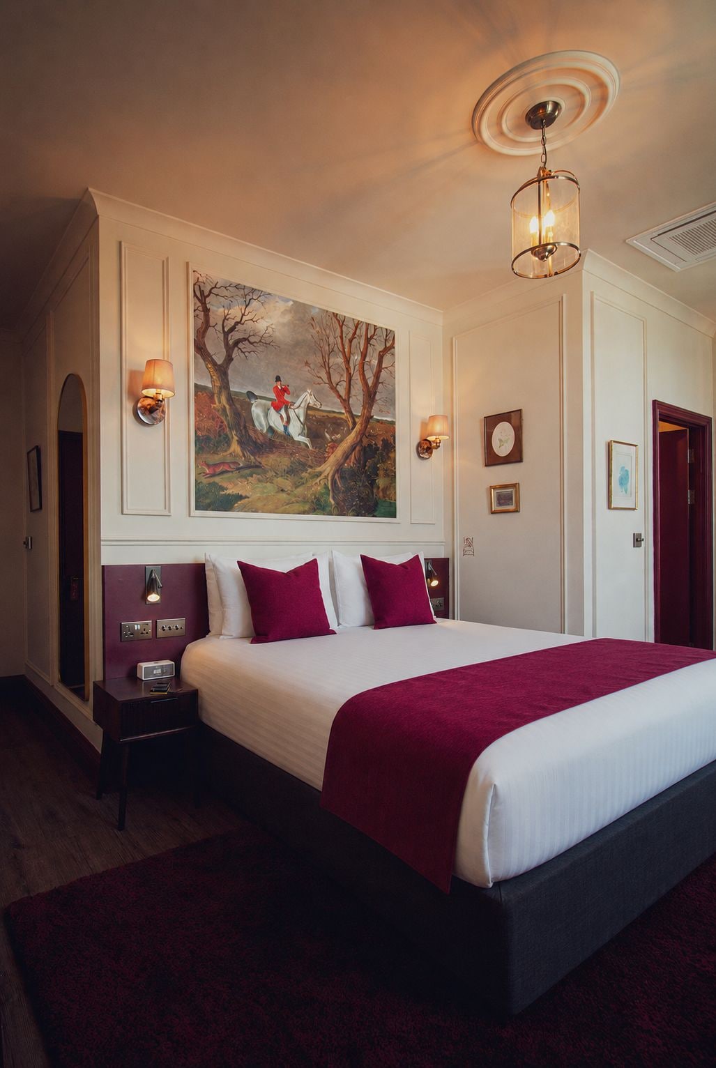 Habitación de hotel con una cama grande, dos mesitas de noche, un cuadro en la pared y una puerta a la derecha.