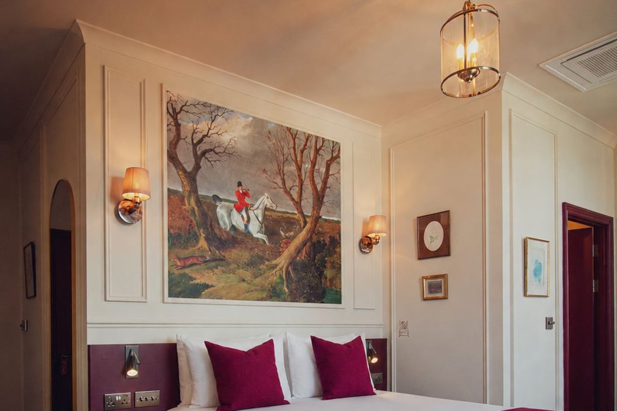 A hotel room with a large bed, two bedside tables, a painting on the wall, and a door to the right.