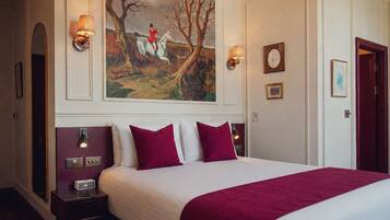Habitación de hotel con una cama grande, dos mesitas de noche, un cuadro en la pared y una puerta a la derecha.