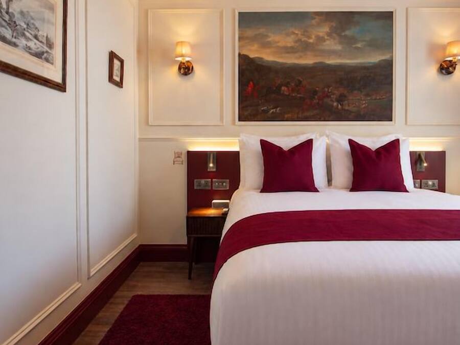 Quarto de hotel com uma cama grande, um tapete vermelho, um quadro na parede e duas luminárias de parede.