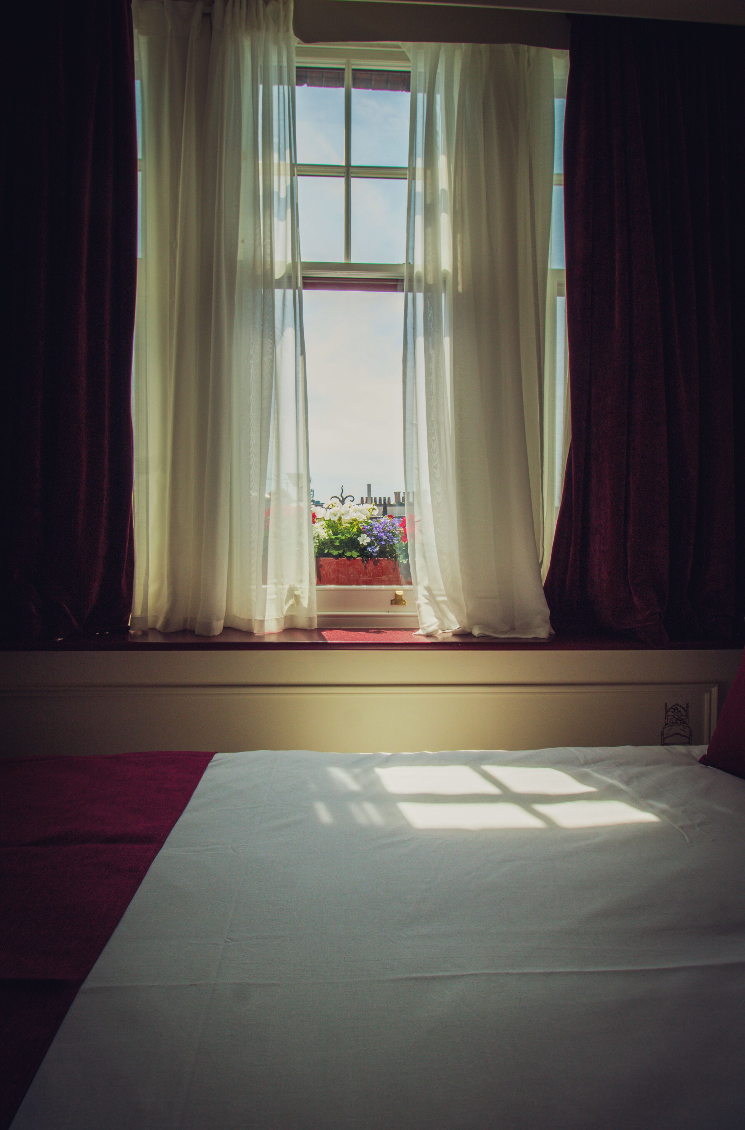 A room with a large window, white curtains, and a view of a balcony with flowers.