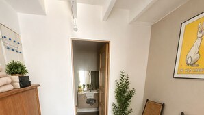 Un couloir avec une armoire en bois, des chaises en osier, une plante en pot et un tableau encadré accroché au mur.