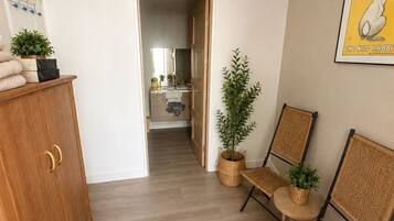Un couloir avec une armoire en bois, des chaises en osier, une plante en pot et un tableau encadré accroché au mur.