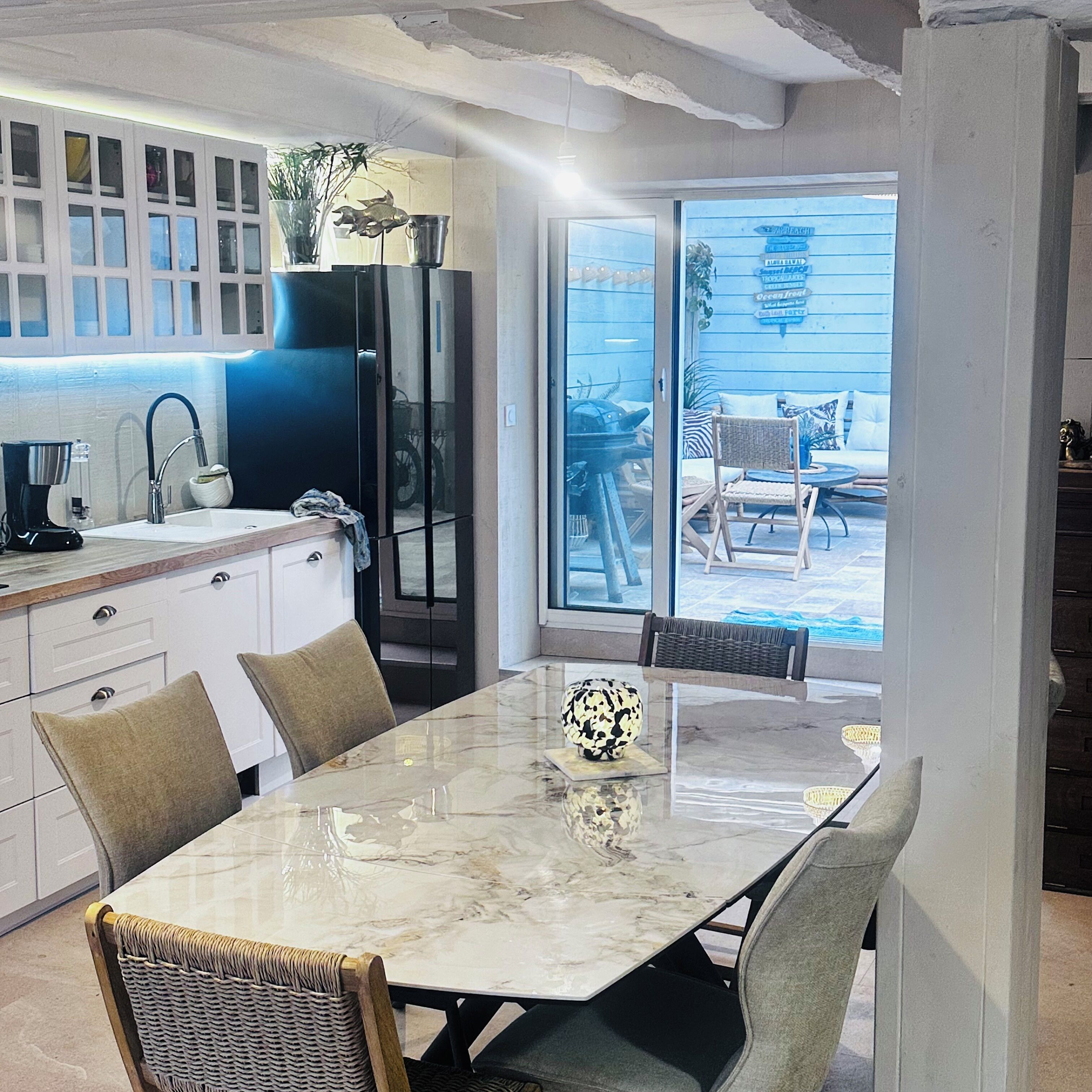 Une cuisine moderne dotée d’un grand îlot central, d’un coin repas avec une table en marbre et d’une vue sur le jardin à travers des portes vitrées.