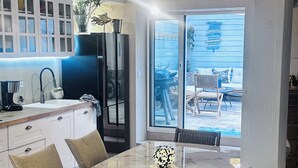 Une cuisine moderne dotée d’un grand îlot central, d’un coin repas avec une table en marbre et d’une vue sur le jardin à travers des portes vitrées.