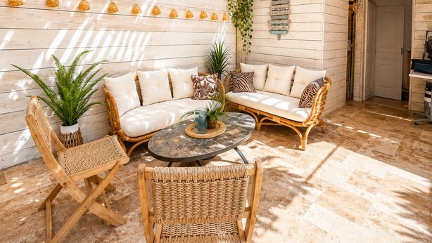 Un espace intérieur accueillant, avec un plafond en bois, un canapé confortable, des fauteuils en osier et une petite table ronde.