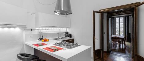 A modern kitchen with a white island, black bar stools, and a large pendant light.