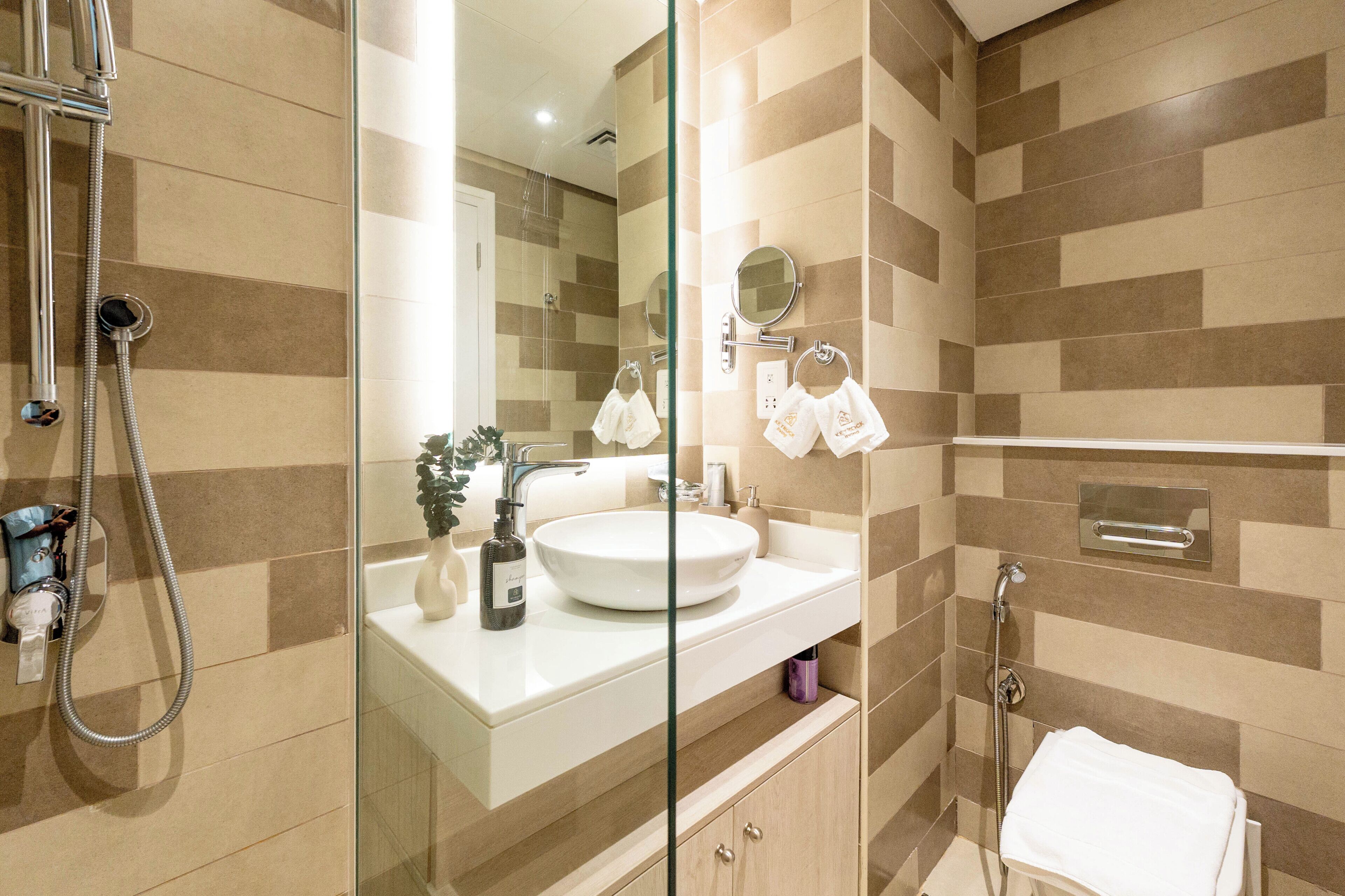 A modern bathroom with a glass shower enclosure, a white sink, and a mirror.