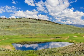 Ein Golfplatz mit Teich, grünen Hügeln und blauem Himmel.