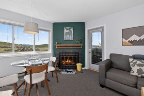 Ein Wohnzimmer mit Kamin, einem gedeckten Esstisch und einer Couch mit Kissenmuster.