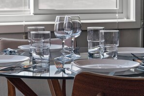 Ein Esszimmertisch ist gedeckt mit klarem Glas, Tellern und Besteck, im Hintergrund ein Fenster.