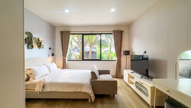 Un dormitorio con cama, televisor, escritorio y ventana con cortinas.