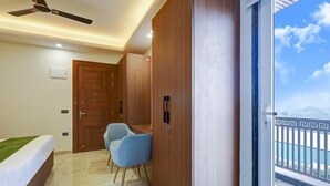 A bedroom with a bed, a desk, a chair, a wardrobe, a ceiling fan, and a balcony with a railing. - Limewood Stay Premium Studios Sector 29 (Gurugram)