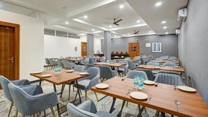 A conference room with multiple tables, chairs, ceiling fans, and recessed lighting. - Limewood Stay Premium Studios Sector 29 (Gurugram)