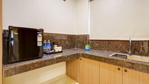 A kitchen with a black refrigerator, granite countertop, wooden cabinets, a sink, and a window with a white blind. - Limewood Stay Premium Studios Sector 29 (Gurugram)