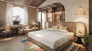 A bedroom with a large bed, a desk, and a chair, with a view of the city through a window.
