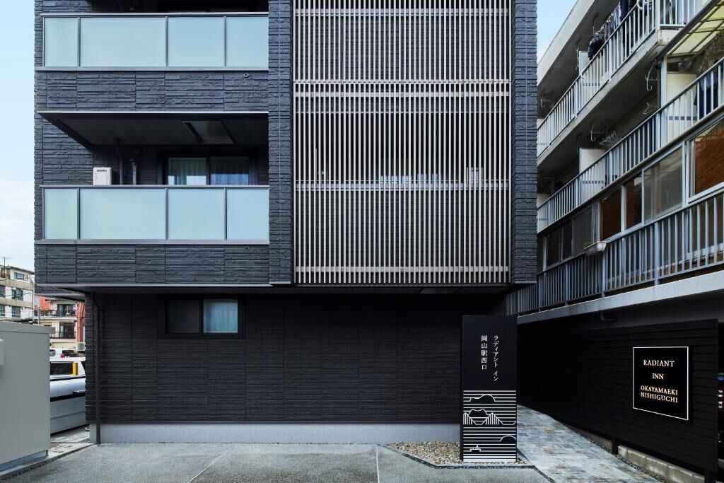 A modern building with a dark facade, multiple balconies, and a sign indicating 'Radiant Inn' in a Japanese city.