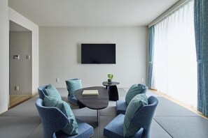 Una habitación moderna con una televisión de pantalla plana, dos sillones azules, una mesita redonda y una planta en maceta.